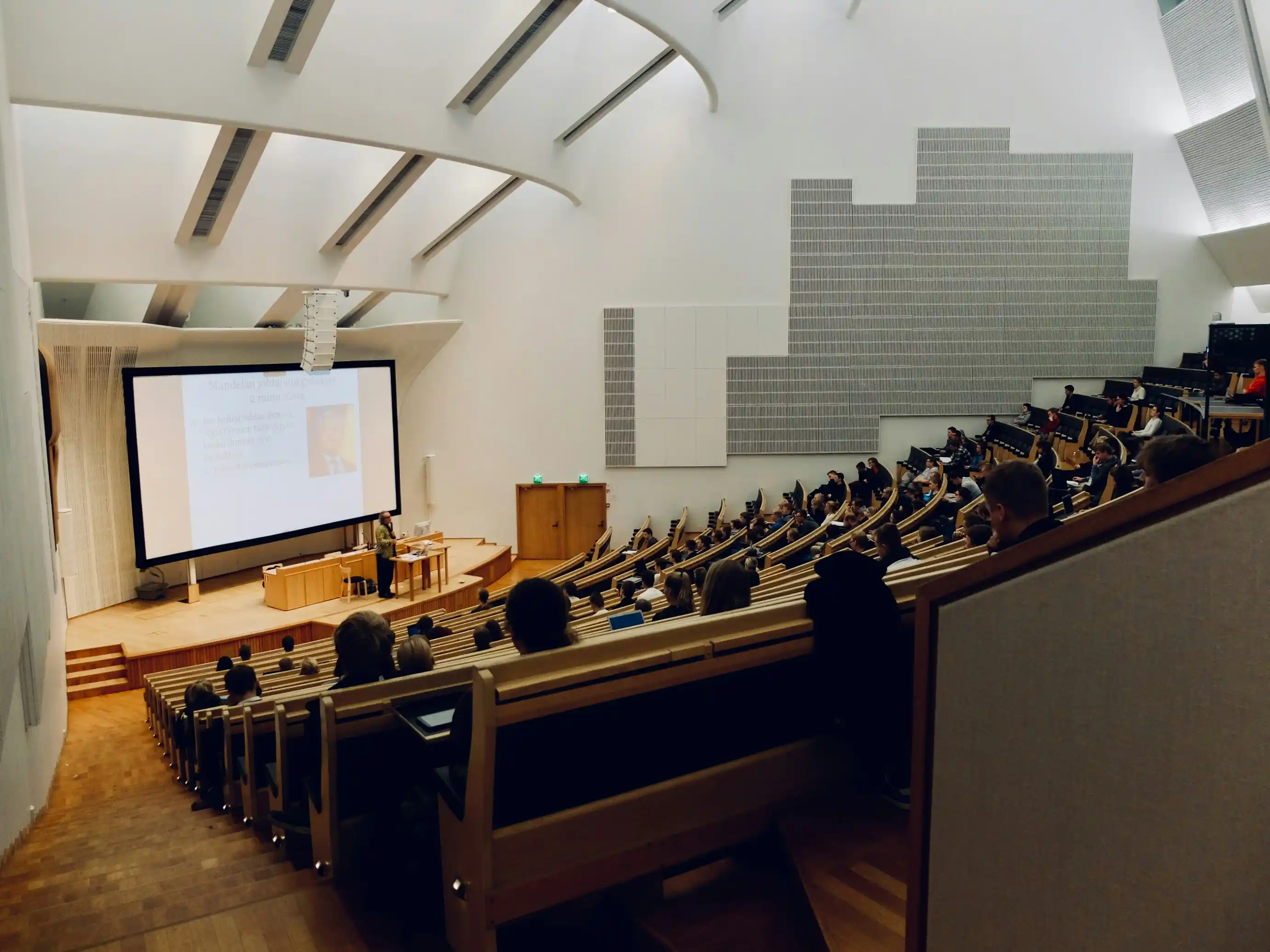 Conf&eacute;rence dans un amphith&eacute;&acirc;tre avec public et &eacute;cran g&eacute;ant.