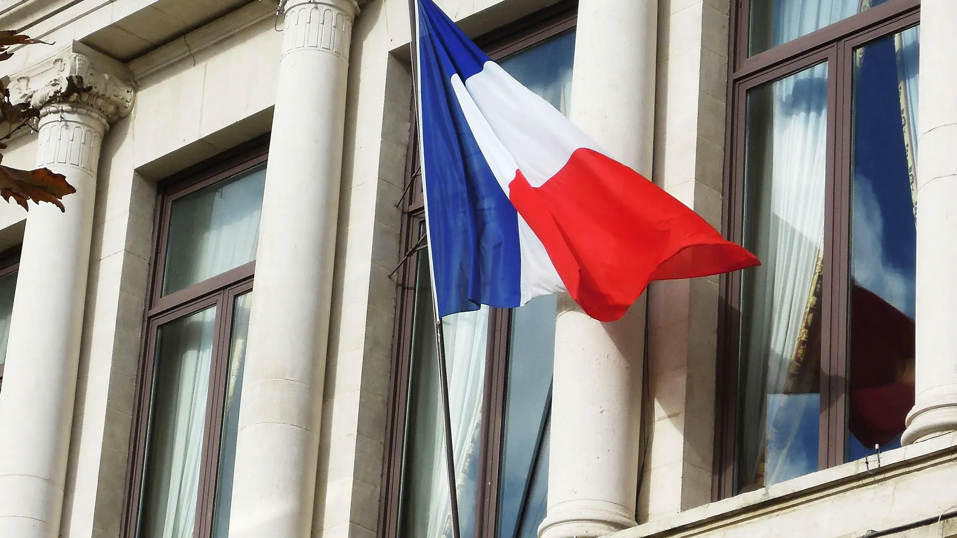 Drapeau fran&ccedil;ais bleu blanc rouge flottant sur la fa&ccedil;ade d&rsquo;un b&acirc;timent officiel en pierre avec colonnes.