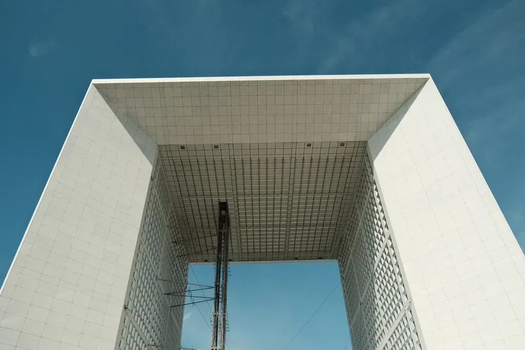 Vue en contre-plong&eacute;e de la Grande Arche de La D&eacute;fense &agrave; Paris, monument moderne en forme de cube &eacute;vid&eacute; sous un ciel bleu clair.