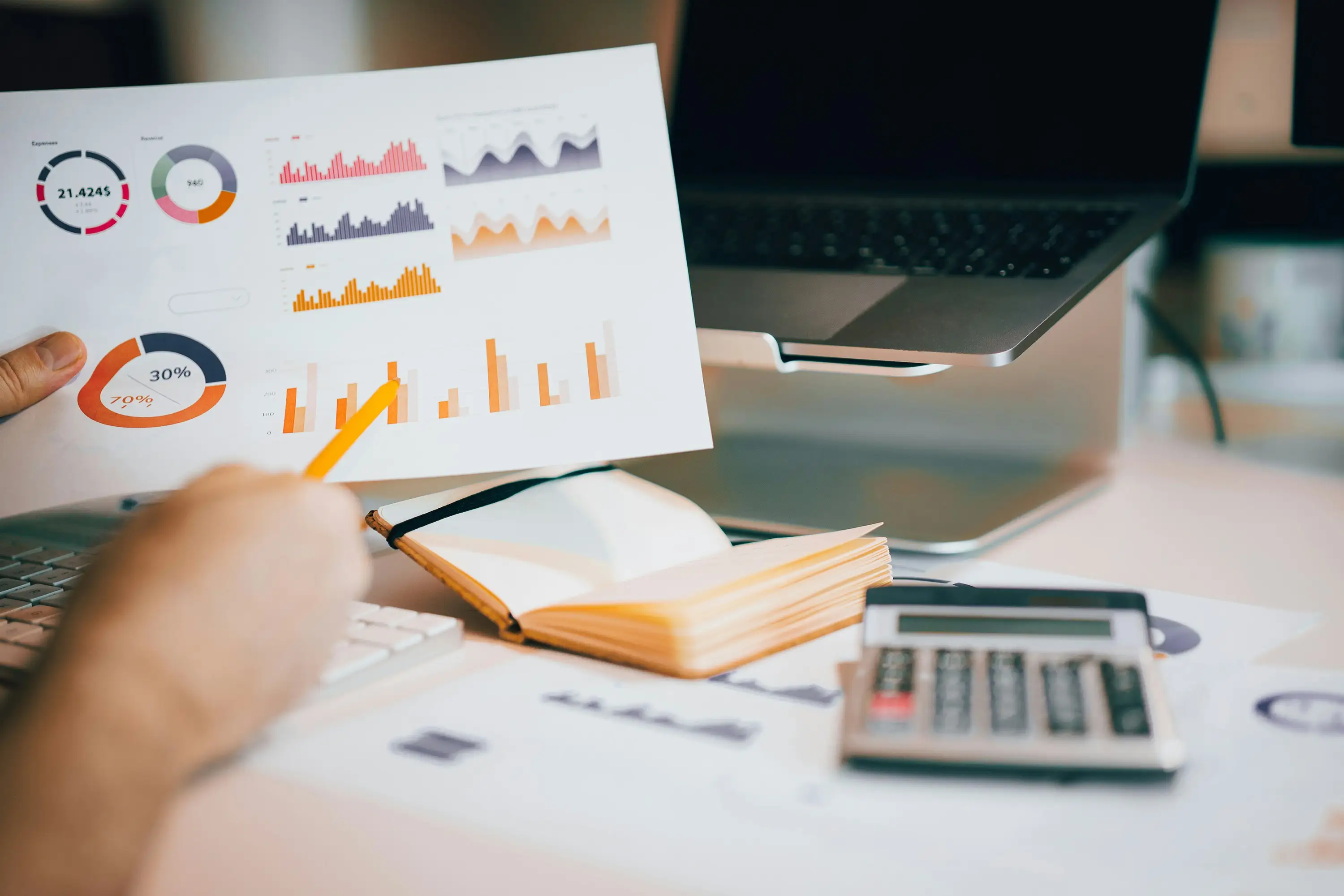 Analyse de graphiques et de donn&eacute;es financi&egrave;res sur un bureau, avec un document de statistiques, un ordinateur portable et une calculatrice.