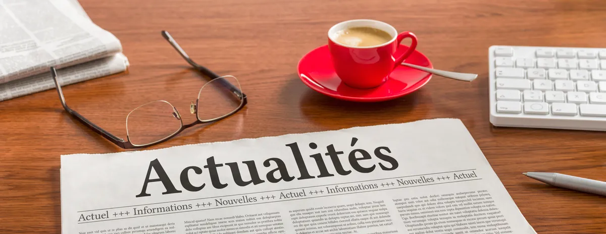 Journal titr&eacute; Actualit&eacute;s pos&eacute; sur un bureau, avec une paire de lunettes et une tasse de caf&eacute;