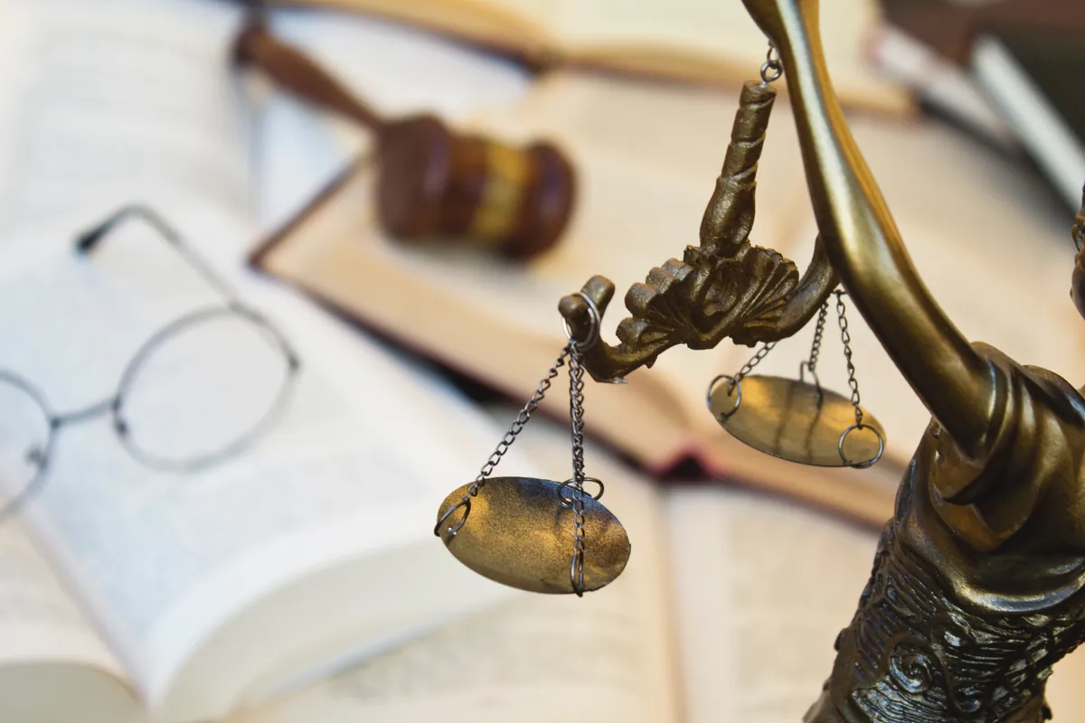Statue de la Justice tenant une balance avec des livres de droit en arri&egrave;re-plan